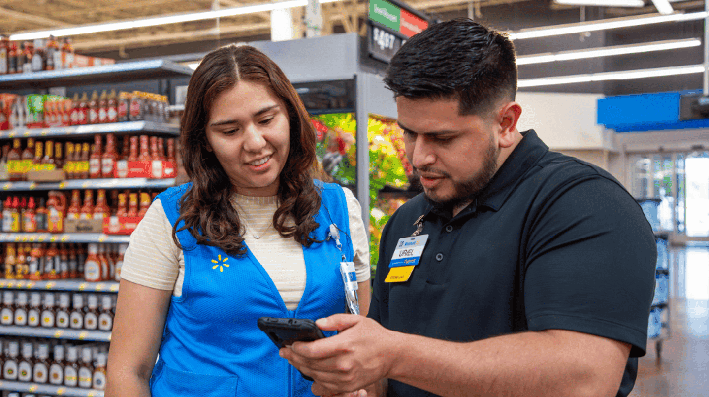 Two store associates checking stock together on a phone in a shop aisle